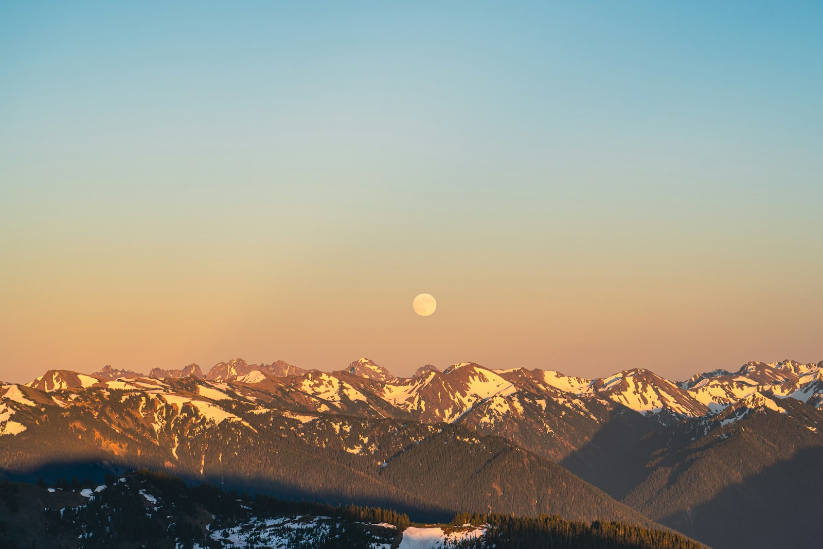 A view of a mountain range with the moon in the distance